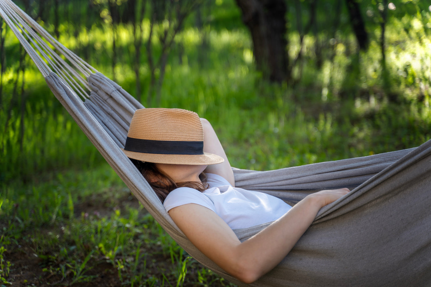 A woman asleep on a hammock with a hat over her face